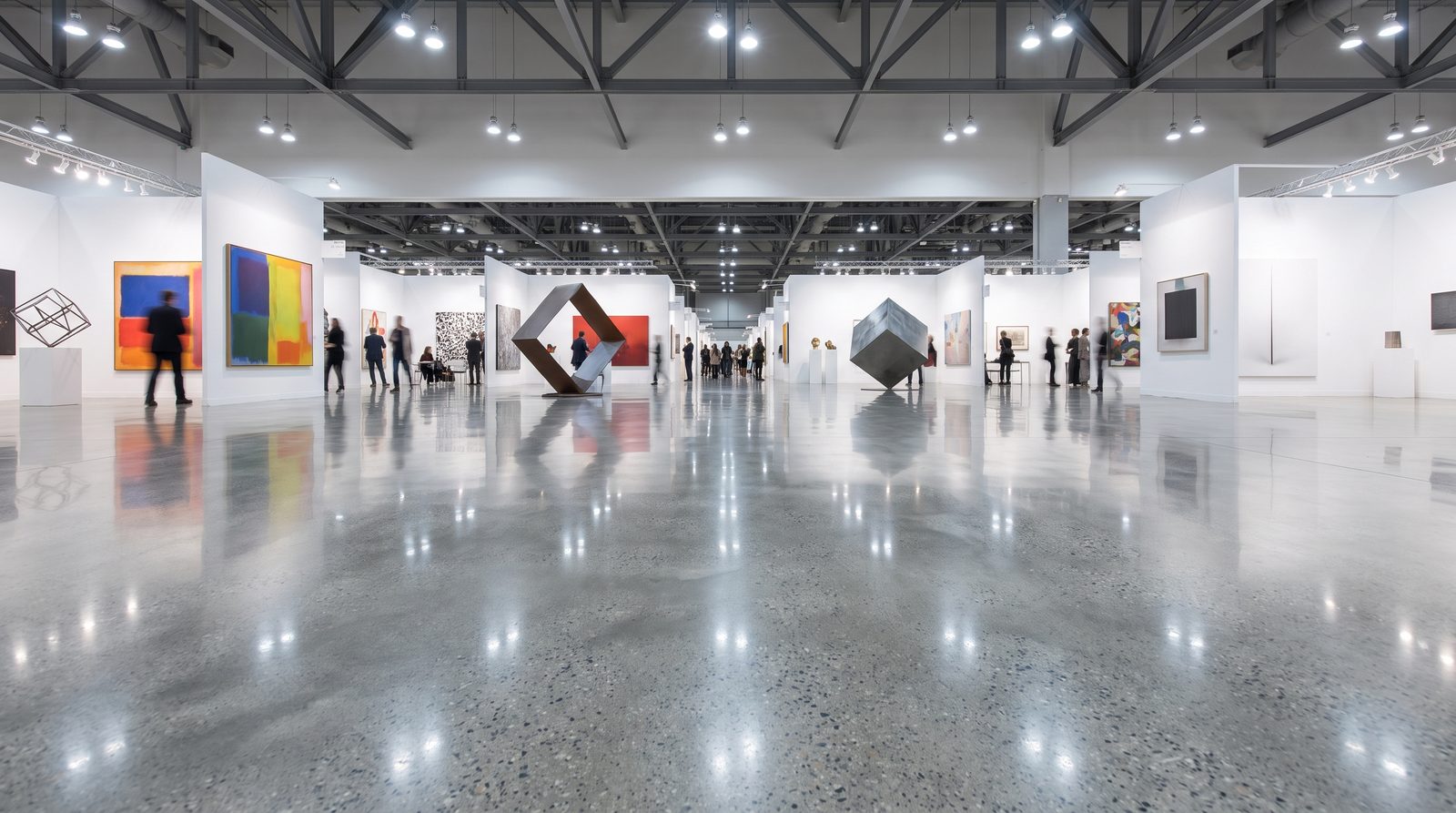 Sanat galerisi ve fuar salonunda stand bölmelerini ve açık çelik makas tavanı yansıtan geniş parlatılmış beton zemin.